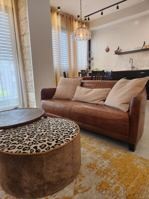 A modern living room with a brown leather sofa, a round ottoman with a leopard print, and a yellow patterned rug. - Rosa's Place (Jerusalem)
