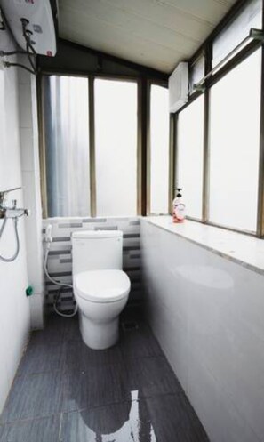 A compact bathroom with a toilet, a shower, and a window.