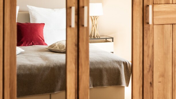 Ein Schlafzimmer mit einem Bett, Kissen, einem Nachttisch mit Lampe und einem Holztürrahmen.