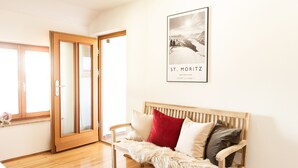 Ein gemütliches Zimmer mit einer hölzernen Bank, einem gerahmten Bild von St. Moritz und einer Glastür zum Balkon.