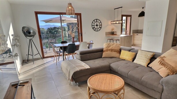 A modern living room with a large sectional sofa, a dining table, and a wicker coffee table.