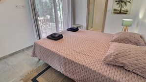 A bedroom with a bed, a small table, a lamp, and a door leading to a balcony.