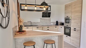 A modern kitchen with a wooden island, two bar stools, a built-in oven, and a microwave.