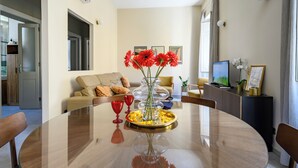 Ein modernes Wohnzimmer mit einem Esstisch mit Glasplatte, einem beigefarbenen Sofa und einem Fernseher.