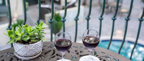 A metal table with two wine glasses and a potted plant on a balcony overlooking a pool.