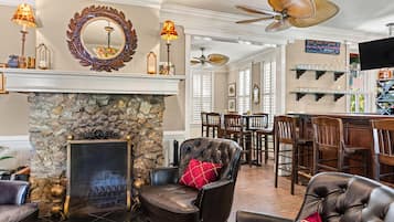A well-appointed living room with a stone fireplace, leather armchairs, and a dining area with wooden chairs and a bar.
