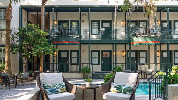 A courtyard with wicker furniture, a pool, and a building with balconies. - Village Inn and Pub - Adults Only (St. Simons Island)