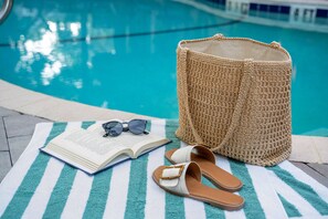 A poolside setting with a striped towel, an open book, a pair of sandals, and a woven bag. - Village Inn and Pub - Adults Only (St. Simons Island)