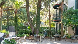 An outdoor patio with a pool, surrounded by lush greenery and shaded by trees. - Village Inn and Pub - Adults Only (St. Simons Island)