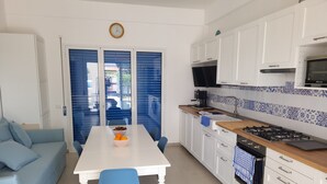 A modern kitchen with white cabinets, a stove, and a microwave. There is a dining table with chairs and a bowl of fruit. - Entire villa, large spaces, 5 minutes walk to the beach suitable for families groups (Villaggio San Leonardo)
