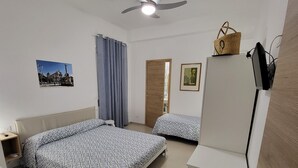 A hotel room with two beds, a ceiling fan, a TV, and a wooden door. - Entire villa, large spaces, 5 minutes walk to the beach suitable for families groups (Villaggio San Leonardo)