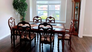 A dining room with a wooden table and chairs, a ceiling fan, and a window with blinds.
