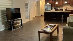 A spacious living room with a flat-screen TV, a coffee table, and a ceiling fan.