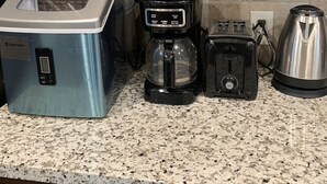 A kitchen with a stainless steel blender, a coffee maker, a toaster, and a kettle on a granite countertop.
