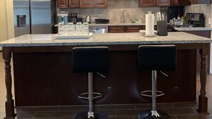 A modern kitchen with dark wood cabinets, a large island with bar stools, stainless steel appliances, and pendant lighting.