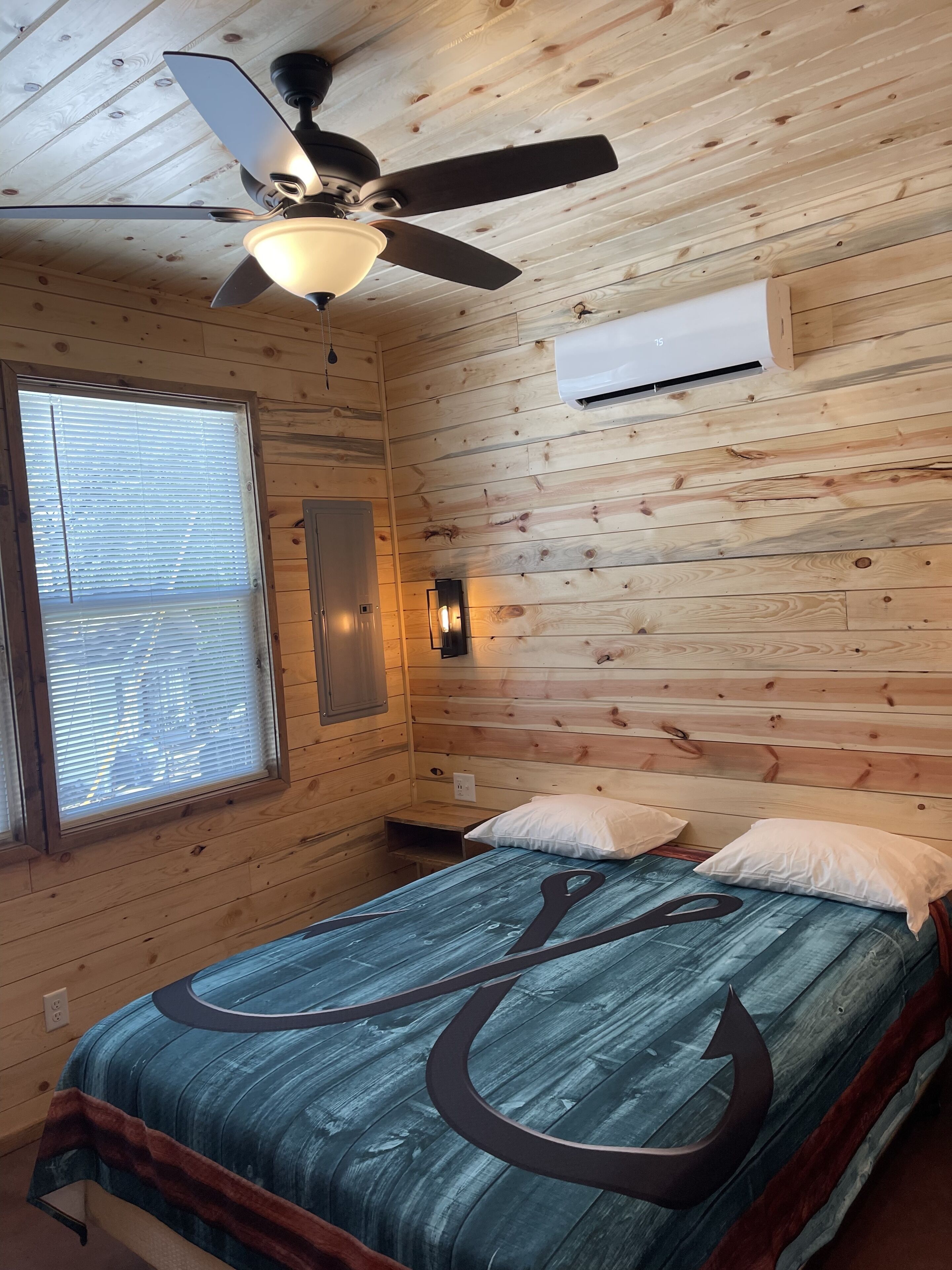 Une pièce de type cabane en bois, comprenant un lit, un ventilateur de plafond, une fenêtre et un climatiseur fixé au mur.