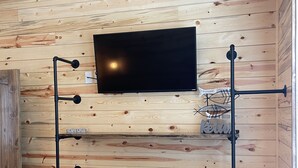 A room with a wooden ceiling and walls, a mounted flat-screen TV, and a metal stand with hooks.