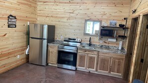 A compact kitchen with wooden walls, a stainless steel refrigerator, a stove, and a microwave.