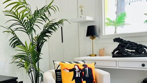 A modern room with a white desk, a small white armchair with a 'Pulp Fiction' pillow, a potted plant, and a lamp. - 5min Palais, Luxury&Cinema Studio,Croisette,Forville,beaches (Cannes)