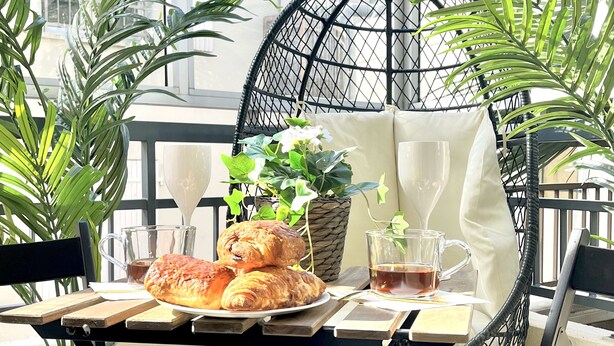 A patio with a round black metal chair, a table with pastries, a potted plant, and a glass of tea. - 5min Palais, Luxury&Cinema Studio,Croisette,Forville,beaches (Cannes)