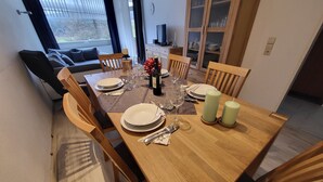 A dining area with a wooden table set for four, surrounded by chairs. A television is mounted on the wall, and a cabinet with glass doors is visible in the background. - Fewo Luchsauge im Ferienresort mit Pool (Schluchsee)