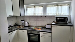 A compact kitchen with white cabinets, a stove, a toaster, and a window with curtains. - Fewo Luchsauge im Ferienresort mit Pool (Schluchsee)