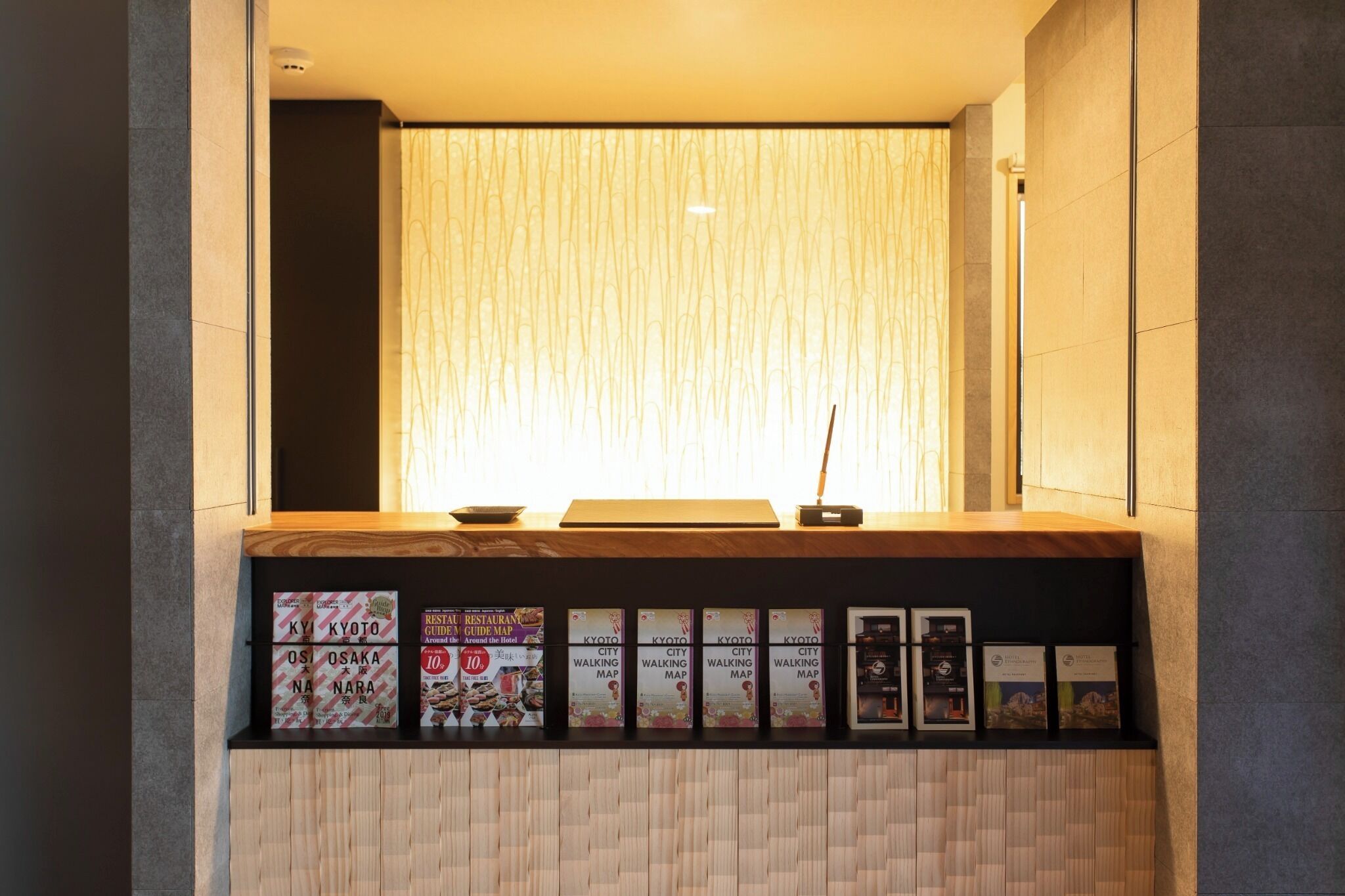 A reception desk with a wooden counter, a standing lamp, and a window with vertical blinds. There are several framed maps and promotional materials on the counter.