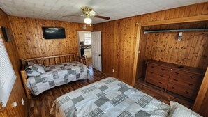 Ein Zimmer mit Holzwänden, einem Bett mit kariertem Überwurf, einem Schminktisch und einem Deckenventilator.