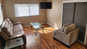Ein Wohnzimmer mit braunem Ledersofa, einem grauen Sessel, einem Glastisch und einem an der Wand befestigten Flachbildfernseher.