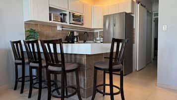 A kitchen with a central island, four bar stools, a refrigerator, and a coffee maker.