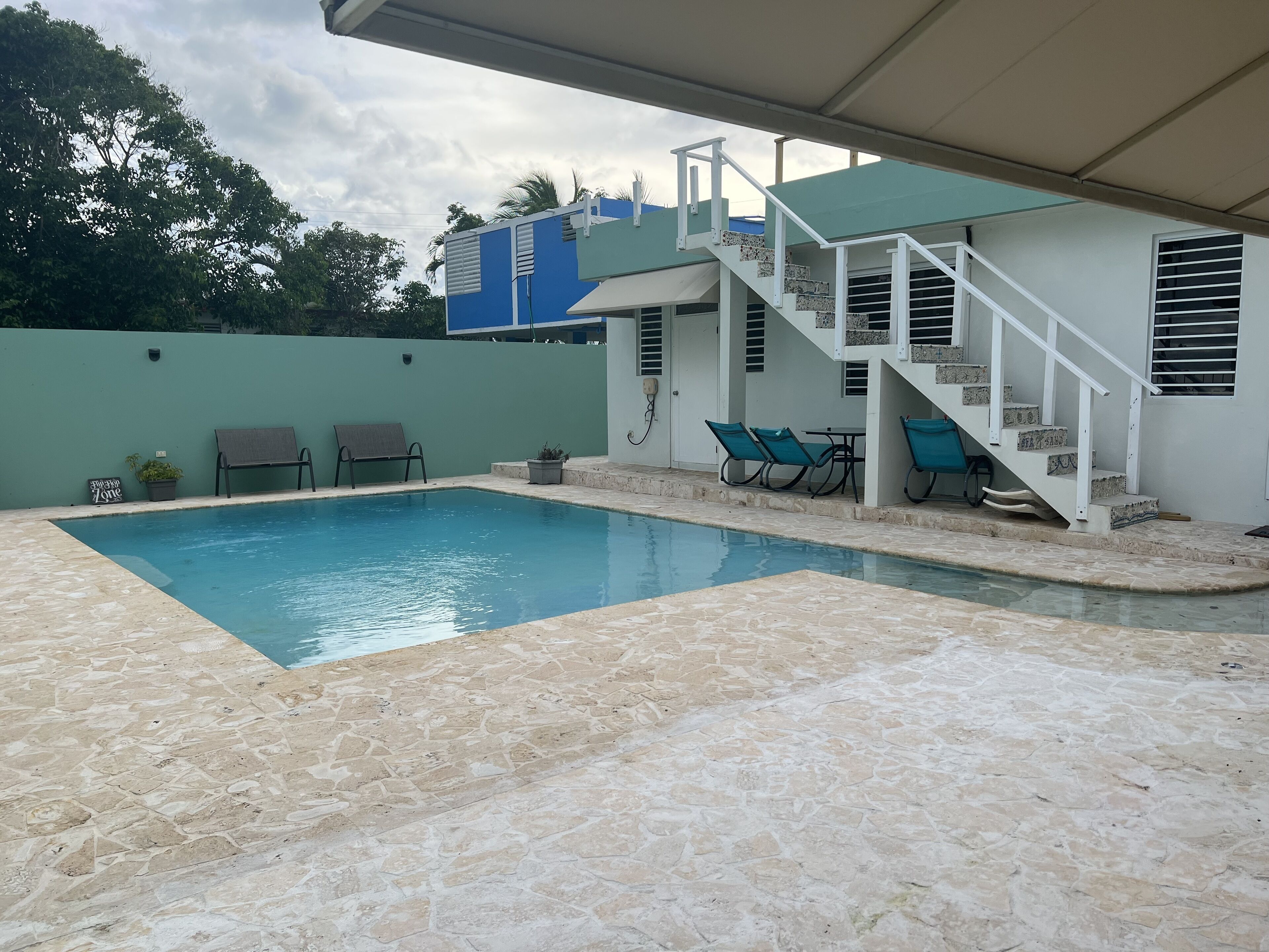 Ein Swimmingpool mit einer Steindekke, einem überdachten Bereich mit Treppe und Außenmöbeln.