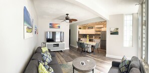 A modern living room with a sofa, TV, and a dining area with chairs and a table.