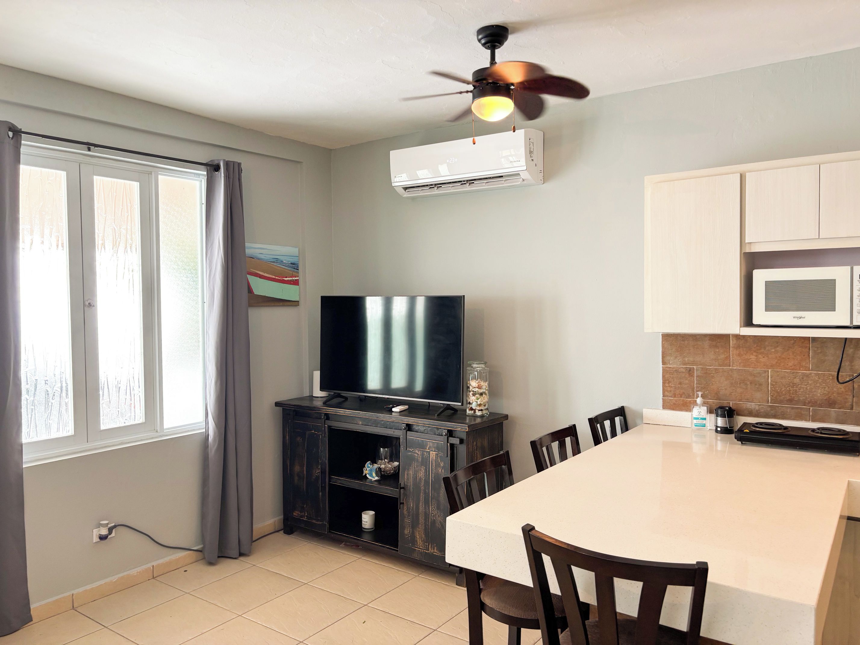 Une cuisine équipée d ’une table à manger, de chaises, d’un climatiseur, d’un ventilateur de plafond et d’un téléviseur.