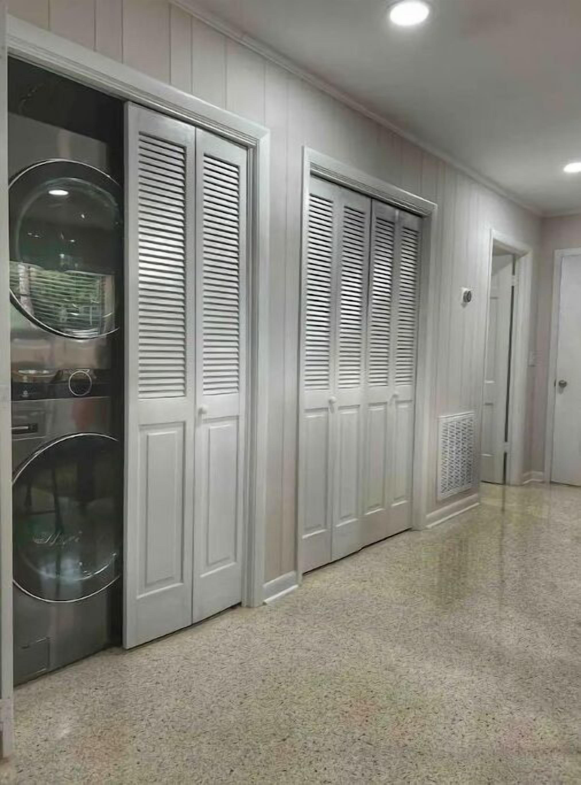 A hallway with white paneled walls and doors, a laundry area with a washing machine, and a radiator on the floor.