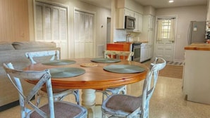 A dining area with a wooden table and four chairs, a kitchen with white cabinets, a microwave, and a refrigerator. - 3 min walk to beach! (Jekyll Island)