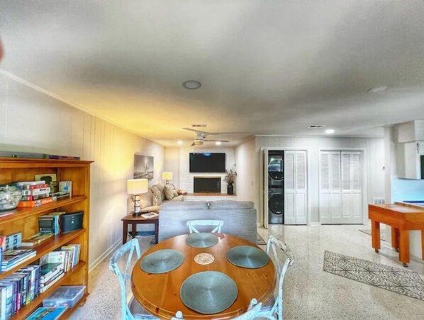 A living room with a dining table, bookshelves, a TV, and a kitchen area with cabinets and a refrigerator.