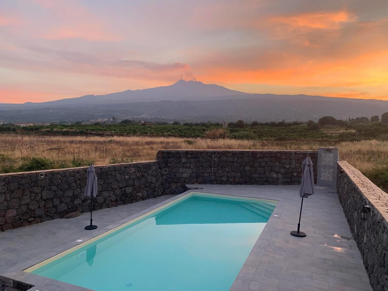 A swimming pool with stone walls and a view of a mountain at sunset.