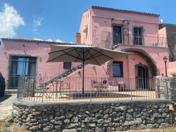 A pink building with a stone wall, a staircase, and outdoor furniture.