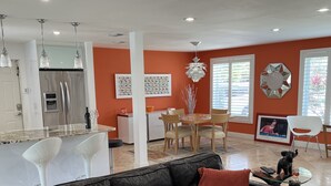 A modern living room with a black leather sofa, a dining area with a white table, and a kitchen with stainless steel appliances.