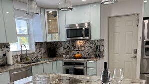 A modern kitchen with a marble island, stainless steel appliances, and white bar stools.