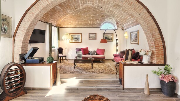 Una sala de estar acogedora con un arco de ladrillo, una mesa de centro de madera, un sofá rojo y una planta grande en maceta.