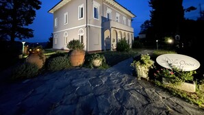 Un edificio de dos pisos con un camino de piedra que lleva a la entrada, rodeado de vegetación y un letrero que dice "Villa Orsini".