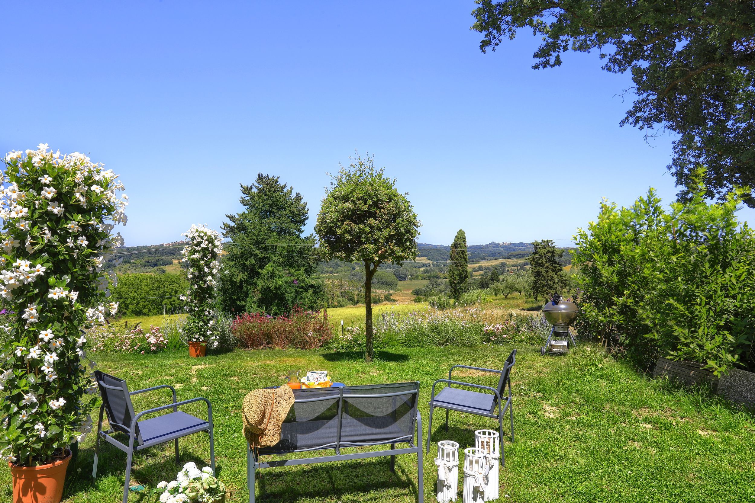 A garden with two metal chairs and a table, surrounded by potted plants and a view of the countryside.