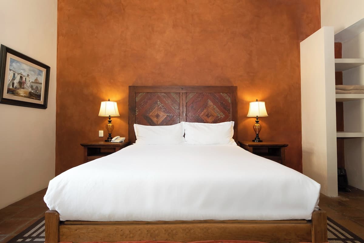 A bed with white linens, two bedside lamps, and a wooden headboard.