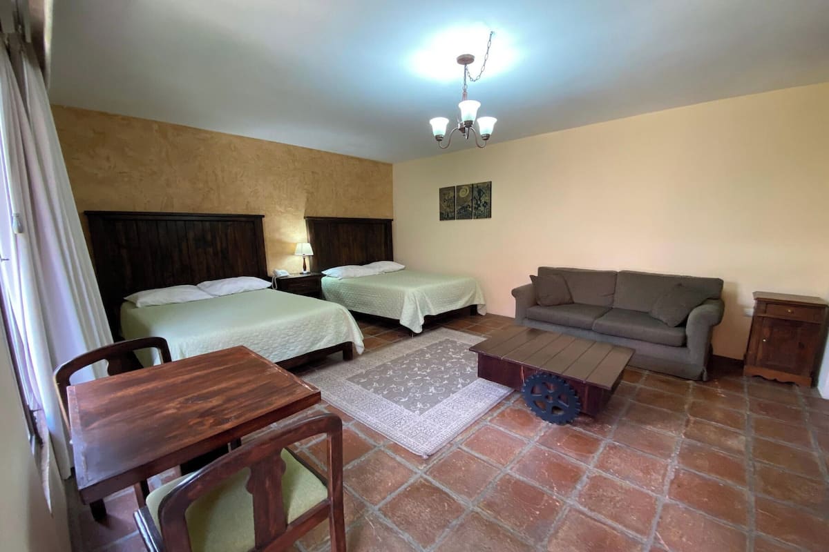 A room with two beds, a sofa, a wooden table, and a patterned rug.