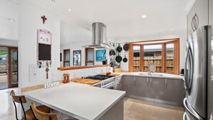 A modern kitchen with a central island, stainless steel appliances, and wooden cabinetry. - Bnbbooking - Burleigh Oasis, heated Spa (Gold Coast)
