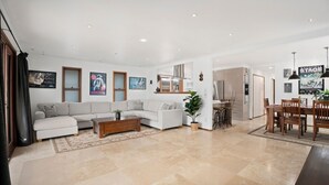 A spacious living room with a sofa set, a coffee table, and a dining area with chairs and a table. - Bnbbooking - Burleigh Oasis, heated Spa (Gold Coast)