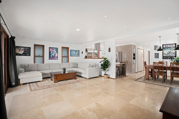A spacious living room with a sofa set, a coffee table, and a dining area with chairs and a table. - Bnbbooking - Burleigh Oasis, heated Spa (Gold Coast)