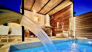 En pool med ett vattenelement, ett trädäck, solstolar och en möblerad sittplats under tak.