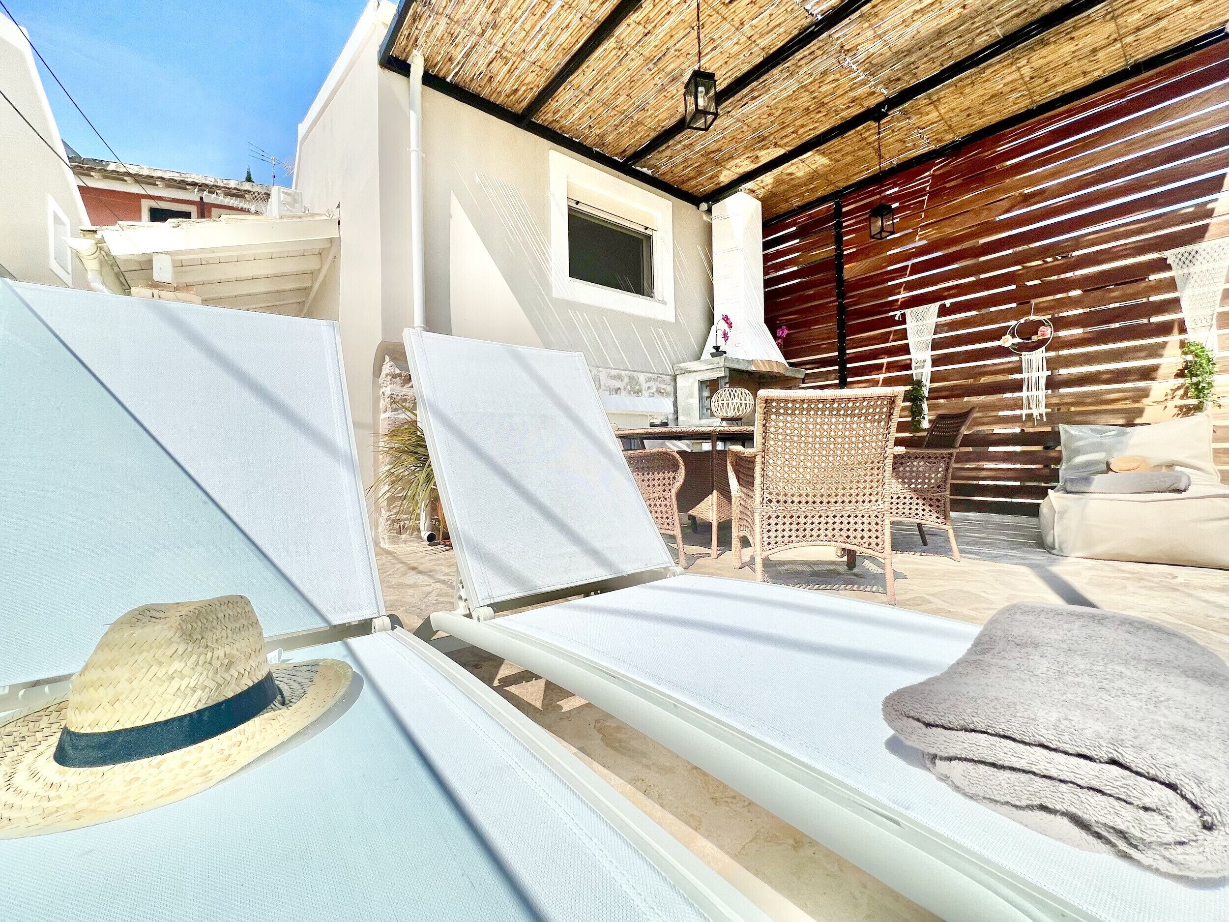 Area relax esterna illuminata dal sole, con poltrone, un tavolo e un tetto di paglia.